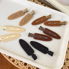 A set of six matte resin side hair clips in various natural and dark brown shades displayed on a white tray.