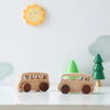 A wooden hand-pushed cart toy for toddlers sits on a white surface next to a yellow sun cutout.