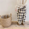 A person wearing beige long sleeves and patterned brown and cream harem pants stands next to a woven basket.