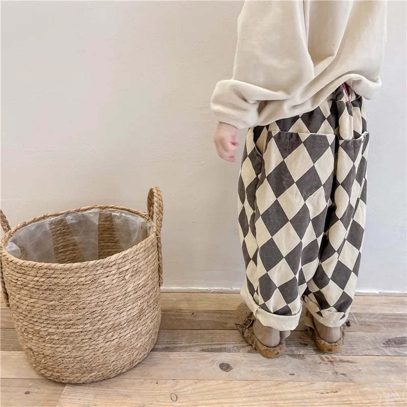 A person wearing beige long sleeves and patterned brown and cream harem pants stands next to a woven basket.