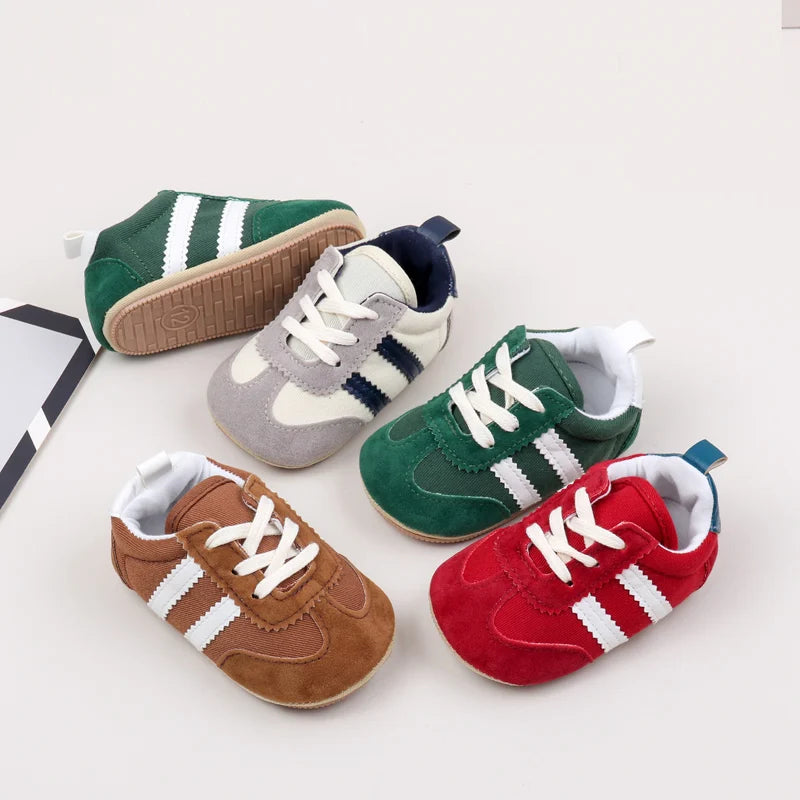 A collection of five baby first walker shoes in various colors and styles, including green, beige, gray, brown, and red.