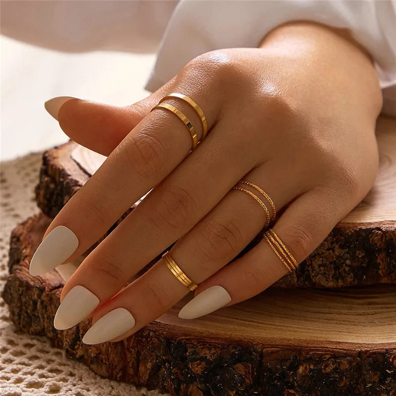 A hand wearing a set of boho gold rings featuring vintage geometric, cross, pearl, and butterfly designs.