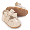 A pair of beige soft non-slip baby first walker shoes with a bow detail and textured sole.