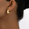 A close-up of vintage gold-plated dome drop earrings worn on a human ear.