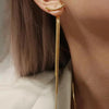 Gold geometric tassel drop earrings hanging from an ear