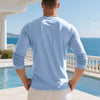 A man wearing a light blue long-sleeve shirt standing outdoors by a pool and ocean view.