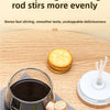 A three-pronged stirring rod is shown next to a mug and round crackers on a wooden table.