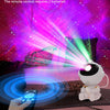 A hand holds a remote control device aimed at an astronaut night light projector displaying galaxy effects.