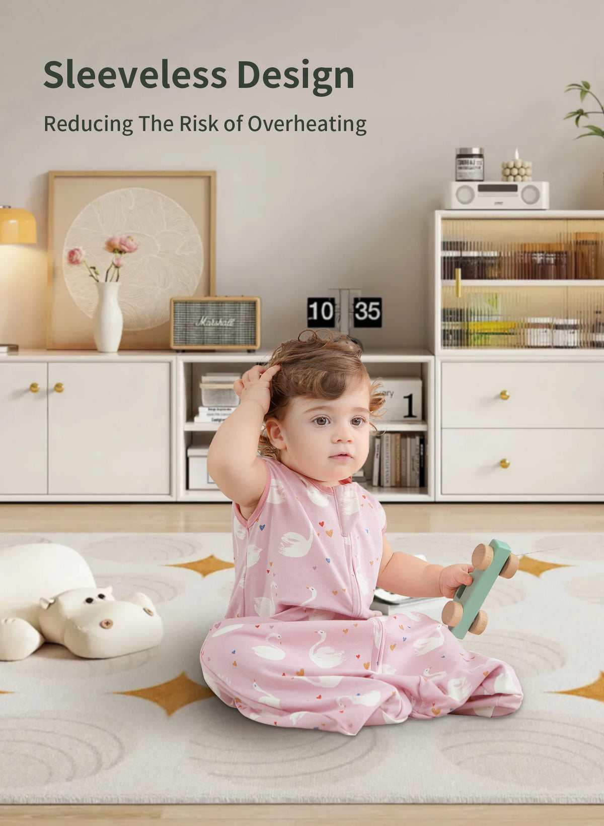 A baby wearing a pink sleeveless sleeping sack is sitting on a rug in a bright room.