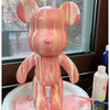 A pink bear figurine painted with marbled orange and yellow stripes, standing in a white dish.