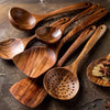 A set of dark brown teak wood cooking utensils, including spoons and a sieve, arranged on a dark surface.