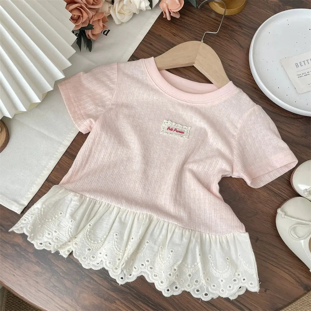 A pink girls cotton short sleeve tee with a lace hem and white trim displayed on a wooden surface.