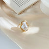 A close-up of a gold starfish pearl ring resting on a soft beige fabric.