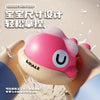 A pink musical light-up whale baby bath toy is shown being held, with water spray visible around it.