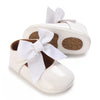 A pair of white baby first walker shoes with white bows and brown non-slip soles.