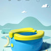A yellow banana-shaped folding toilet for children is shown on a light blue surface with a green mountain background.
