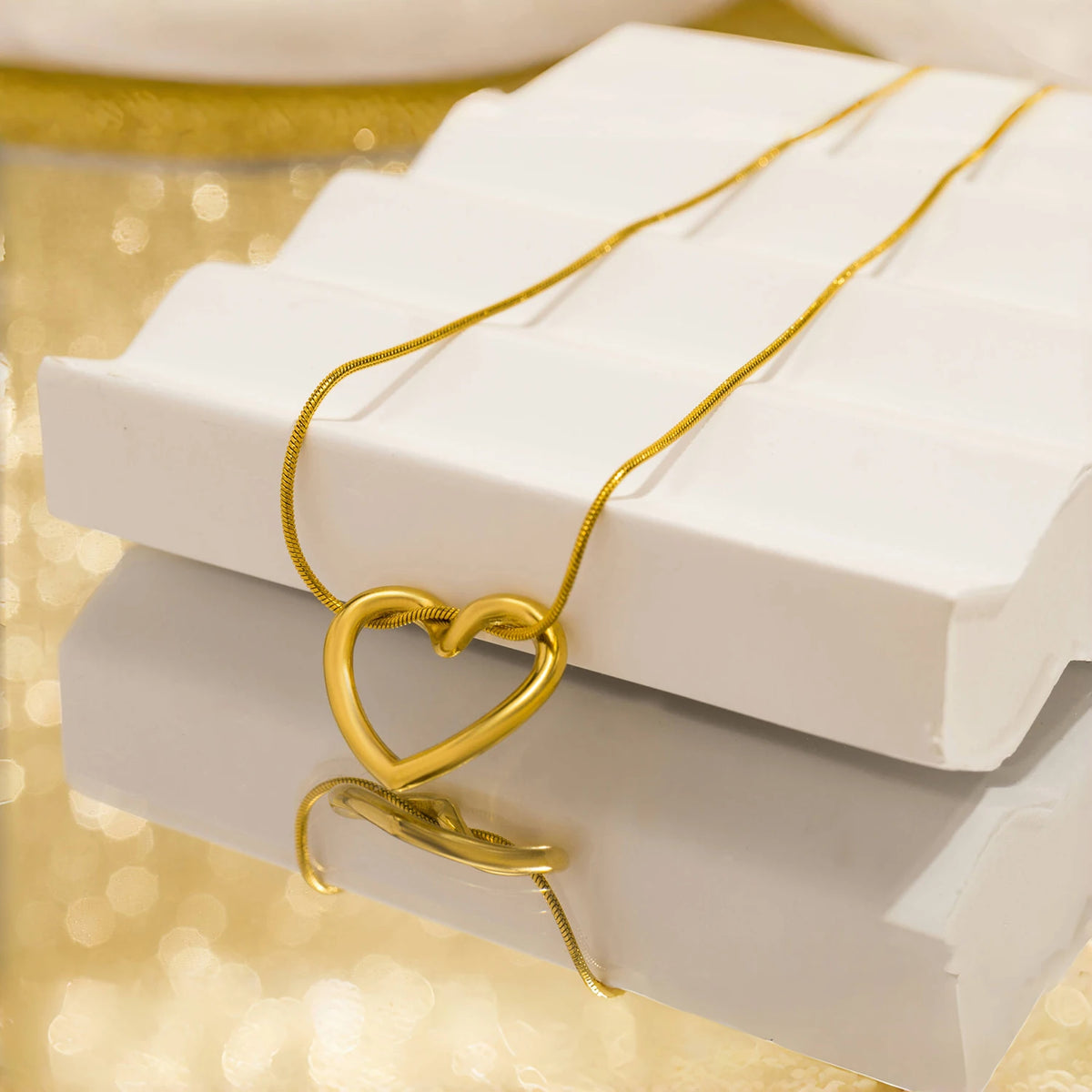 A dainty gold heart pendant necklace with a snake chain resting on white boxes.