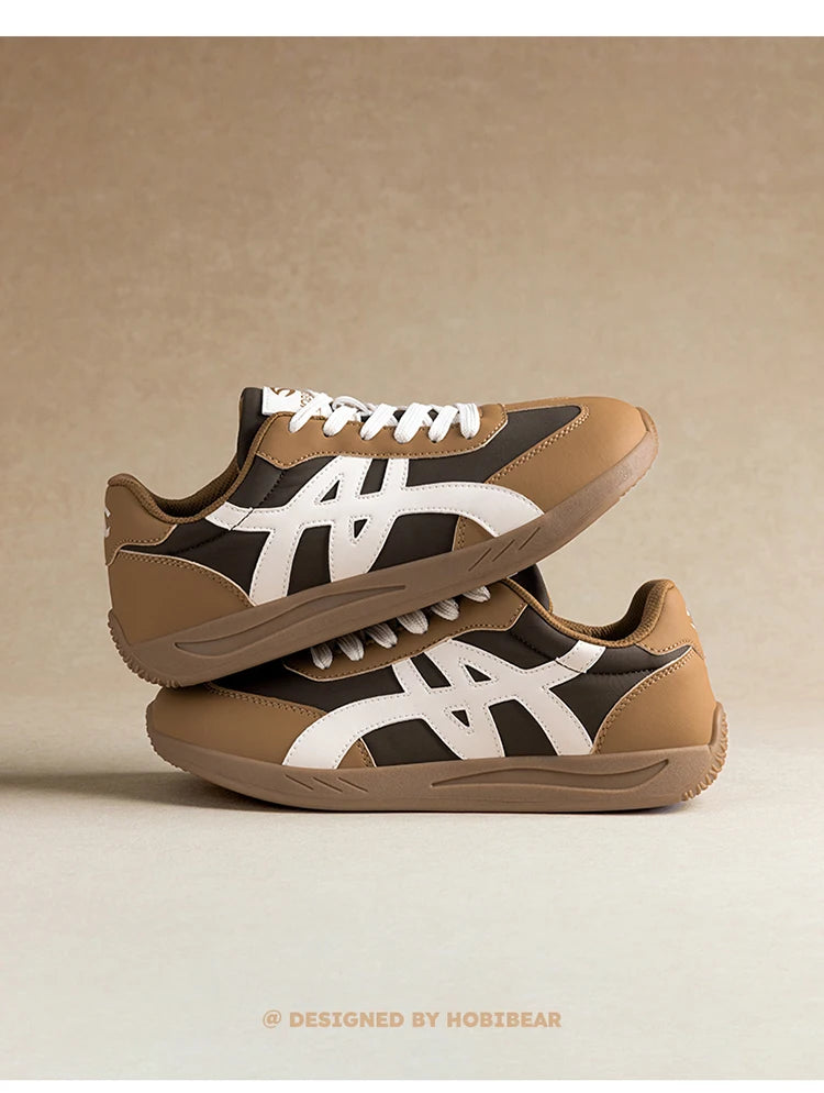 Ein Paar braune und beige minimalistische Sneaker mit weißen Akzenten, von der Seite gezeigt.
