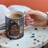 Hånd som holder en keramisk kaffekopp med bilde av en rustikk, smuldrende bokhylle.