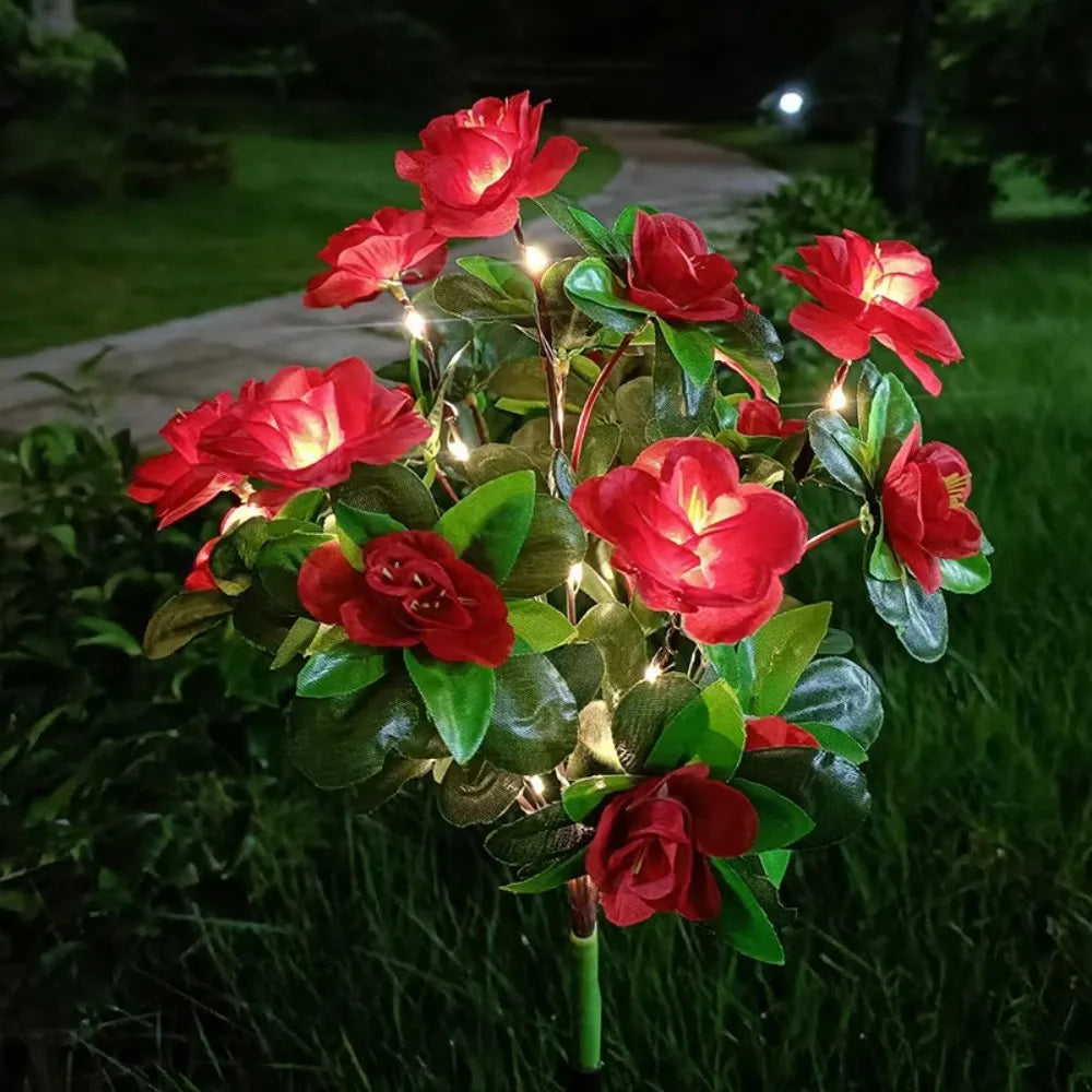 Ein Büschel leuchtend roter Rosen und grünes Laub, von warmen LED-Lichtern in einem Garten erhellt.