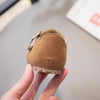 A hand holds a tan retro non-slip kids' moccasin shoe with an easy hook-and-loop closure.