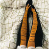 Paar schwarze kniehohe Socken mit orangefarbenem Hühnermuster am Bein, auf einem weiß karierten Laken liegend.