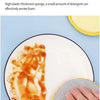 A hand is using a yellow scouring pad to clean greasy stains from food on a white plate.