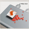 A silicone feeding placemat is shown with a reddish stain being wiped clean by a white cloth, demonstrating its cleaning abil