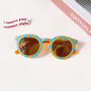 A pair of kids polarized sunglasses with a yellow-orange lens and a blue and yellow patterned frame resting on a white surfac