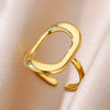 Nahaufnahme eines mehrlagigen geometrischen offenen Rings in Goldtönen auf einem weichen, hellrosa Stoff.