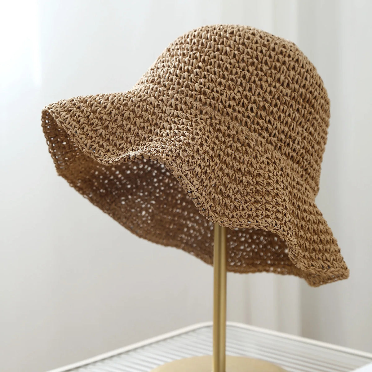 A woven straw crochet fisherman hat with a wide brim displayed on a stand.