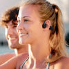 A blonde woman wearing bone conduction sports headphones smiles outdoors.
