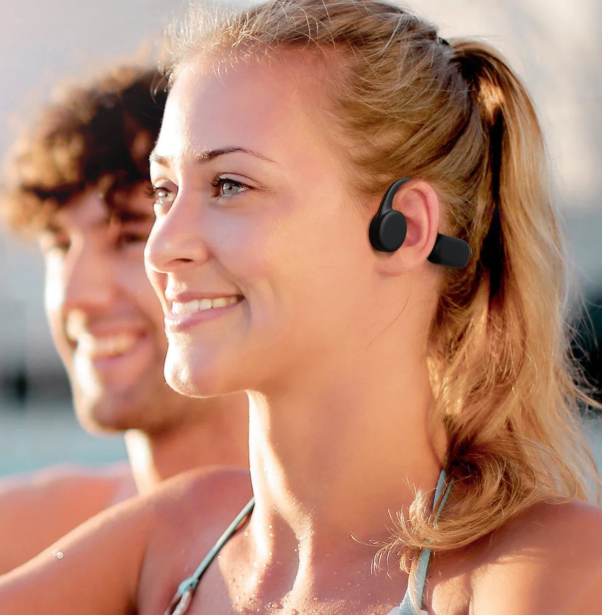 A blonde woman wearing bone conduction sports headphones smiles outdoors.
