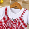 A red and white plaid girls' cotton knit dress with a bow accent displayed on a wooden hanger.