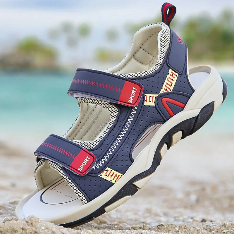 A pair of navy blue and beige breathable summer sport sandals with adjustable straps resting on a sandy beach.