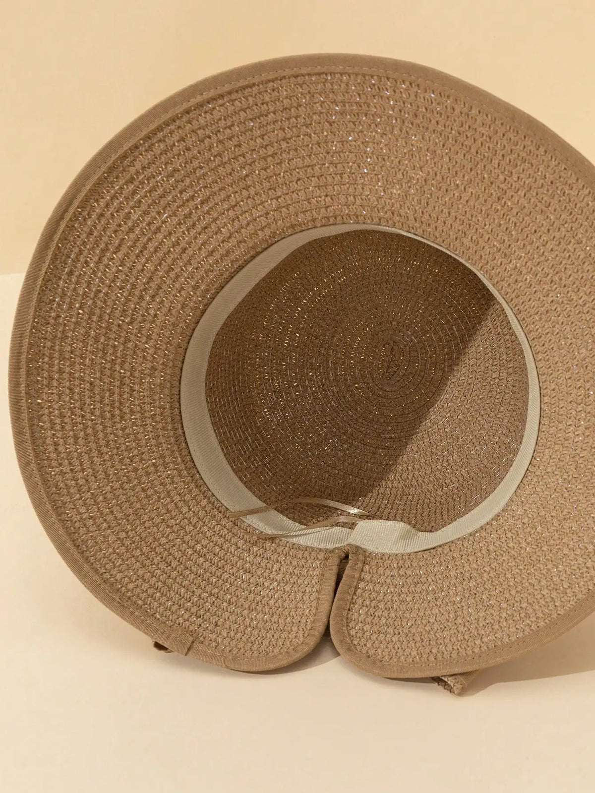 A close-up view of an elegant straw sun hat in a beige color with a woven texture.