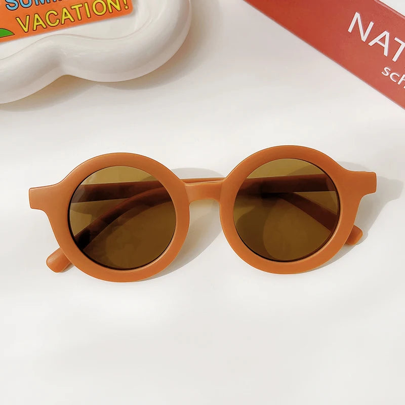 A pair of orange-framed sunglasses with brown lenses resting on a white surface.