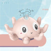 A pink musical whale bath toy with a light-up water spray is shown resting on a surface.