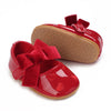 A pair of red baby first walker shoes with a textured sole and a satin bow detail.