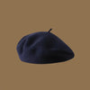 A dark navy blue wool beret hat resting on a plain brown background.