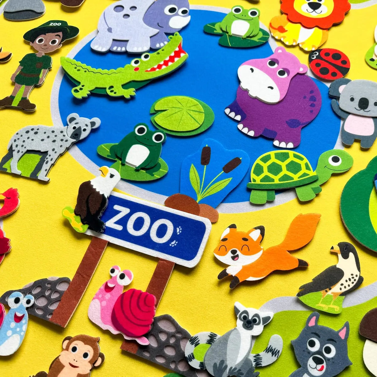 A colorful felt story board set featuring various zoo animals like a purple monkey, green crocodile, and gray bear on a yello