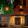 A solar powered metal hanging lantern for outdoor decor is displayed on a wooden surface and a house exterior.