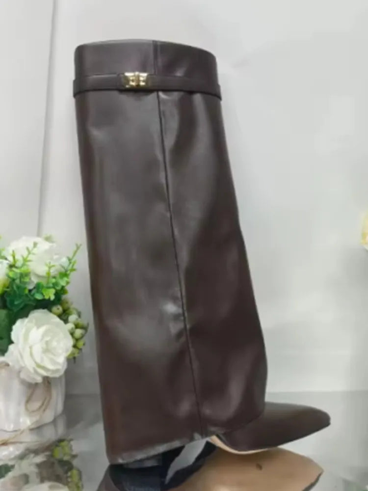 A pair of brown leather knee-high chunky heel boots with a metal buckle displayed on a stand.