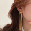 Gold geometric tassel drop earrings worn by a woman with long brown hair