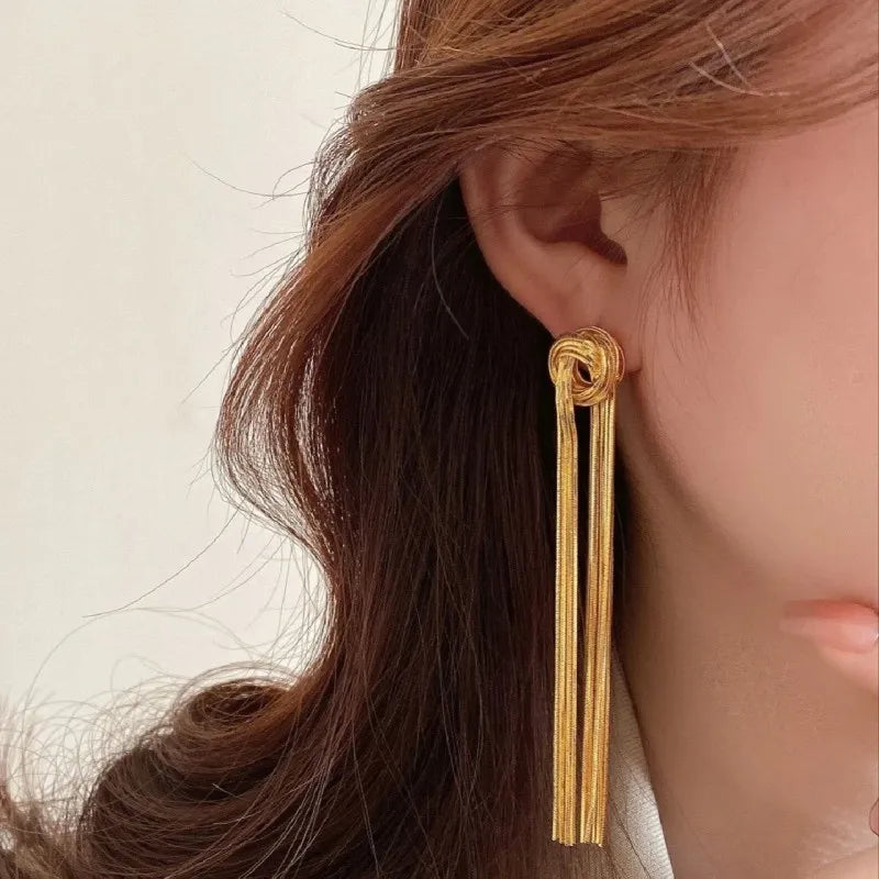 Gold geometric tassel drop earrings worn by a woman with long brown hair