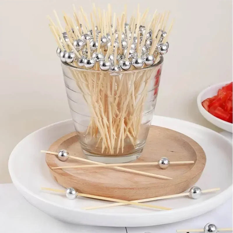 A glass container filled with elegant pearl bamboo skewers for party appetizers and desserts resting on a wooden board.