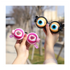 A person holds a pair of novelty funny glasses with large, expressive eyes in a pink and black frame.