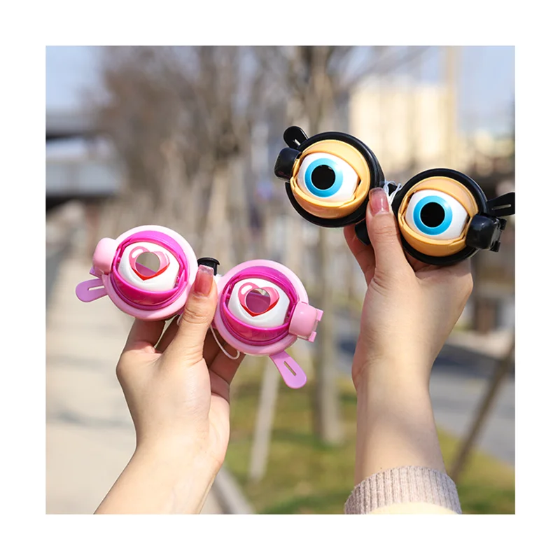 A person holds a pair of novelty funny glasses with large, expressive eyes in a pink and black frame.