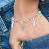 Primer plano de un brazalete de nombre de acero inoxidable bañado en oro, con cadena ajustable y dijes, usado en la muñeca de
