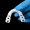 A hand wearing a blue glove holds a clear cosmetic denture teeth kit, shaped like an arc.